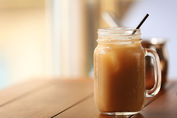 Iced coffee in glass jar with straw on brown wooden table