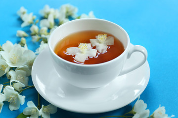 Cup of tea with jasmine flowers on blue background