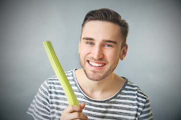 Handsome man eating celery on grey background