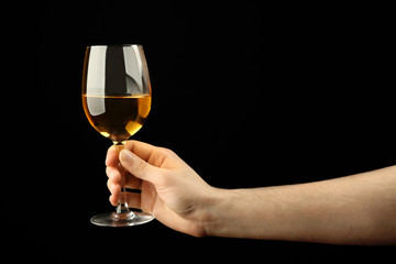 Male hand holding glass of wine on black background