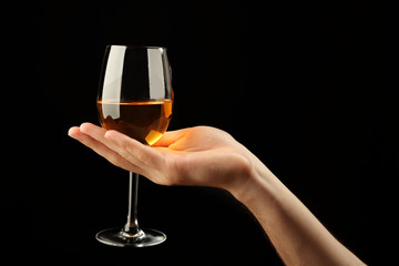 Male hand holding glass of wine on black background