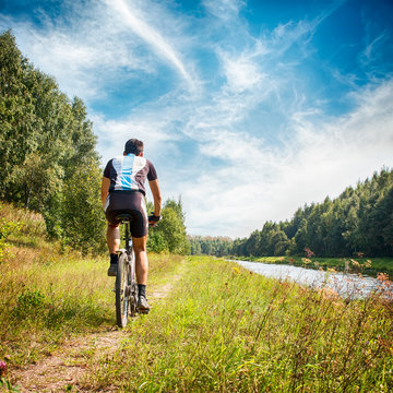 Man Riding a Bicycle on River Bank. Summer Photo.