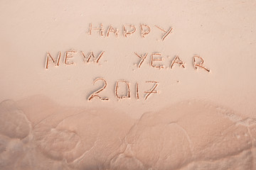 Fototapeta na wymiar 2016 2017 inscription written in the wet yellow beach sand being washed with sea water wave. Concept of celebrating the New Year at some exotic place