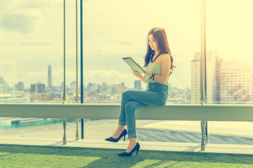 Beautiful Young Asian women using a tablet sitting on the stairs with happiness and concentrate.Vintage tone with city view background.