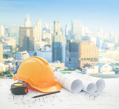 architectural blueprint with safety helmet and tools over modern business district with high building