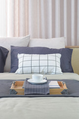 cup of tea and wooden tray setting on bed with classic color scheme bedding 