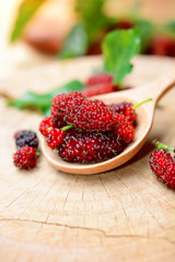 fresh red mulberries with green and yellow mulberry leaf on wooden background.