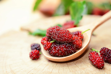 fresh red mulberries with green and yellow mulberry leaf on wooden background.