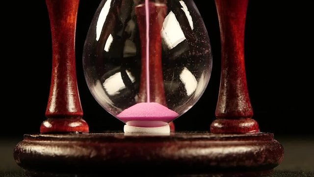 Sand flowing in hourglass. Black. Slow motion. Close up