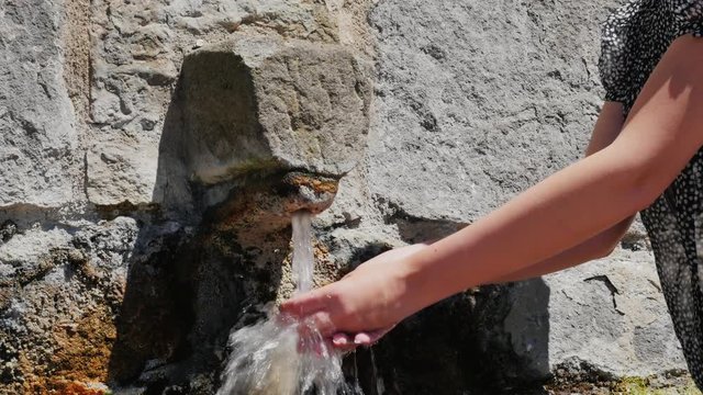 Woman tourist washes his hands of the old stone crane. In the town of Rupit, Catalonia