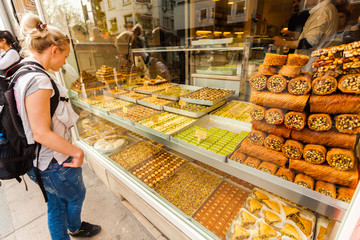 Showcase with Oriental sweets with nuts in assortment. Tourist female standing and looking in the window with oriental sweets on the streets of Istanbul. Shop with sweets. Travel Turkey.