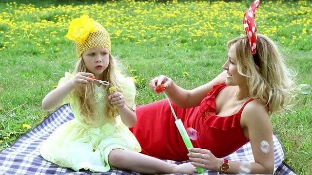 Beautiful woman and girl outdoors blowing bubbles, lying in the grass,smiling.