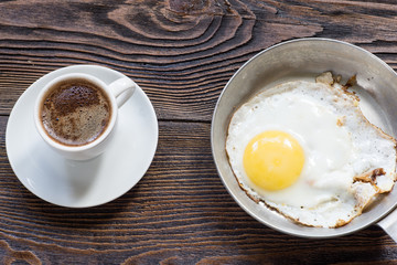 Fried egg on the pan and white  cup of coffee for breakfast.