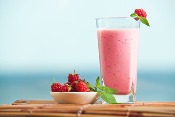 Closeup of raspberry milkshake with mint in glass standing on wooden table. Healthe drink in summer, fresh berry drink.