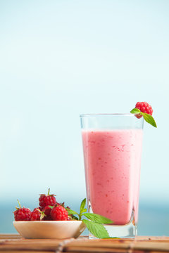 Closeup of raspberry milkshake with mint in glass standing on wooden table. Healthe drink in summer, fresh berry drink.