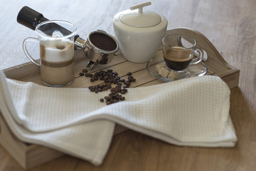 Wooden tray with glass of latte macchiato, espresso, grouphead, coffee beans and brown sugar