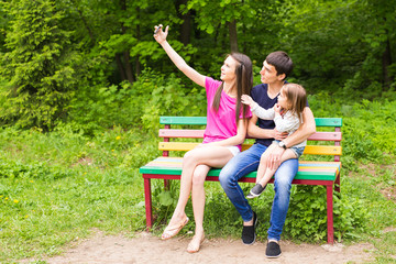 Summer scene of Happy young family taking selfies with her smartphone in the park