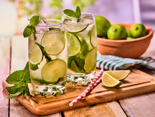 Alcohol country cocktail. On wooden boards two glasses with alcohol cocktail and ice cubes. Drink hundred ninety cocktail mohito with straw and lime bowl and mint leaf. Country outdoor.