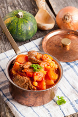 stew of beef with vegetables in a copper pot closeup