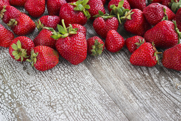 Fresh strawberry harvest scattered on rustic wooden table