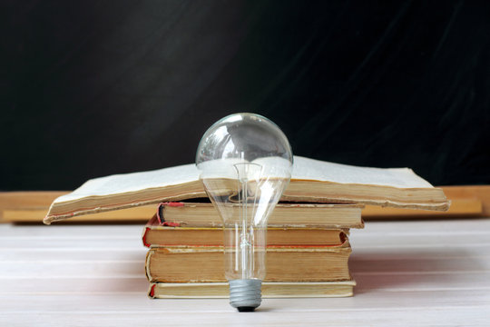 waiting for creative ideas/ electric light bulb standing in front of an open book on the background of blackboard 