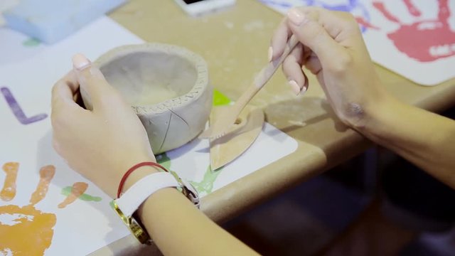 Closeup of hands of young woman ceramist working and finishing pot with white clay in workshop