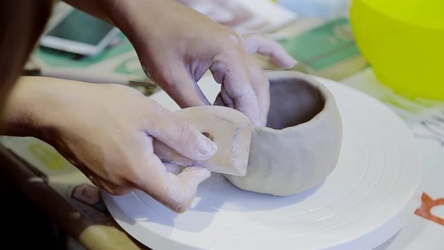 Closeup of hands of young woman ceramist sculpts pot with white clay in workshop