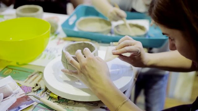 Hands of young woman ceramist working and finishing pot with white clay in workshop