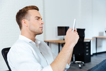 Serious conentrated young businessman sitting and using tablet