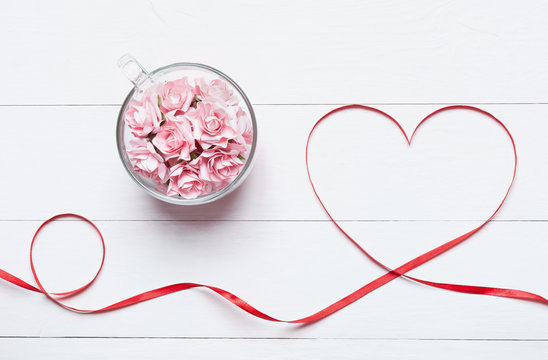 Glass cup full of pink roses with red heart shaped ribbon