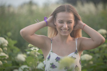 young beautiful woman in the warm rays of the evening sun walking on a green field with white flowers.