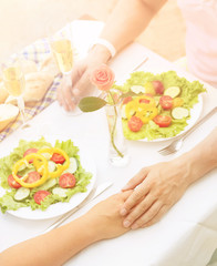 Fototapeta premium Toned picture of beautiful couple holding hands and having lunch or dinner in restaurant or cafe. Man and woman resting spending free time all together on sunny day.