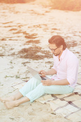 Toned picture of middle-aged poet working on his laptop computer. Handsome businessman in glasses making diagrams for new projects in evening near by sea.