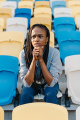 Sporty african american woman sitting on tribune and feeling disappointed against empty stadium
