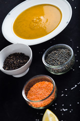 Cream soup of assorted lentil. Yellow and green lens, spices as raw for meal and lemon on black background. Healthy, appetizing, delicious, vegetarian food. Top view, copy space.
