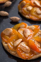 Tart with apricot and apple. Traditional french pie with fruits on dark marble background. Decorated almonds and mint leafs. Delicious dessert with copy space closeup.
