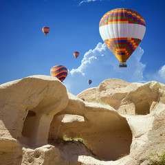Hand carved rooms in limestone rocks near Goreme, Cappadocia. Colorful hot air balloons flies in blue sky in Kapadokya, Turkey