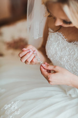 Unrecognizable bride in white dress holding beautiful earrings in hands.