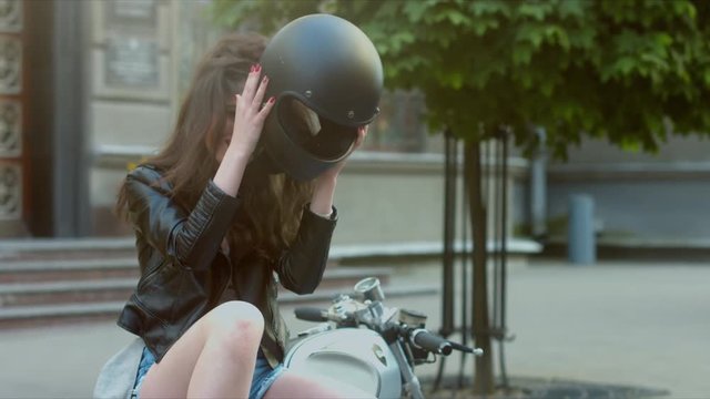 MED Urban portrait of a beautiful Caucasian girl on a motorcycle. Gorgeous brunette female in leather jacket, taking off motorcycle helmet, then laughs. 60 FPS 4K UHD