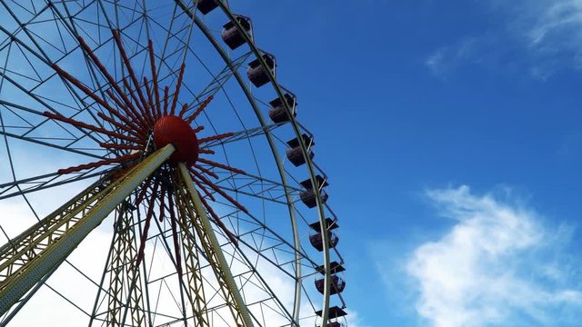 Bottom view on the Ferris wheel. Against the backdrop of a blue sky with clouds