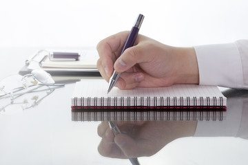 Businessman write a short note on opened notebook with pen and glasses.