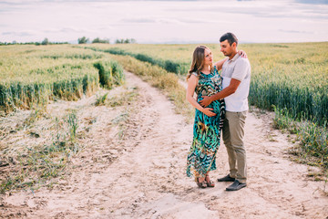 husband and his pregnant wife are walking at sunset in field on the outside. theme romantic pregnancy outdoors.