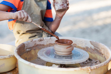 Fototapeta na wymiar Hands of young potter, creating an earthen jar on the circle, cl