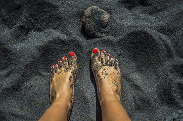 Female bare feet with red nails on black sand beach