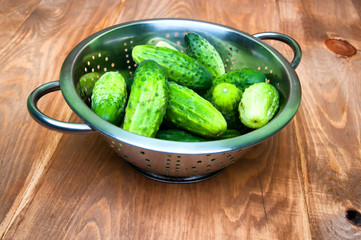 Mini cucumbers in colander on table