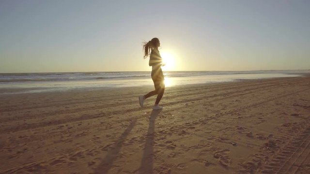 Chica joven corriendo en camara lenta al atardecer en la playa