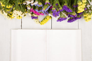 Beautiful colorful flowers and open blank book on a white wooden
