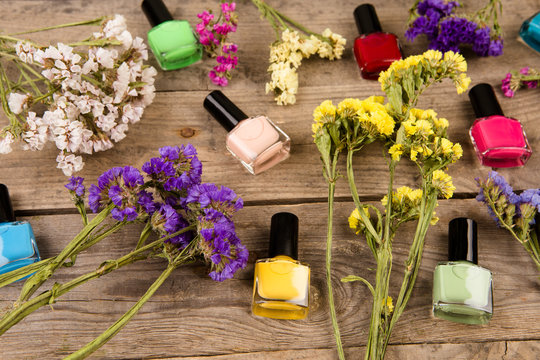 Bottles of colorful nail polish and flowers on brown wooden table
