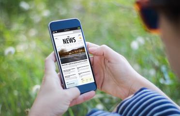 girl in grass holding her news smartphone