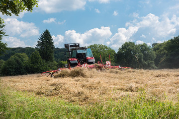 tractor with tedder turning hay on the meadow